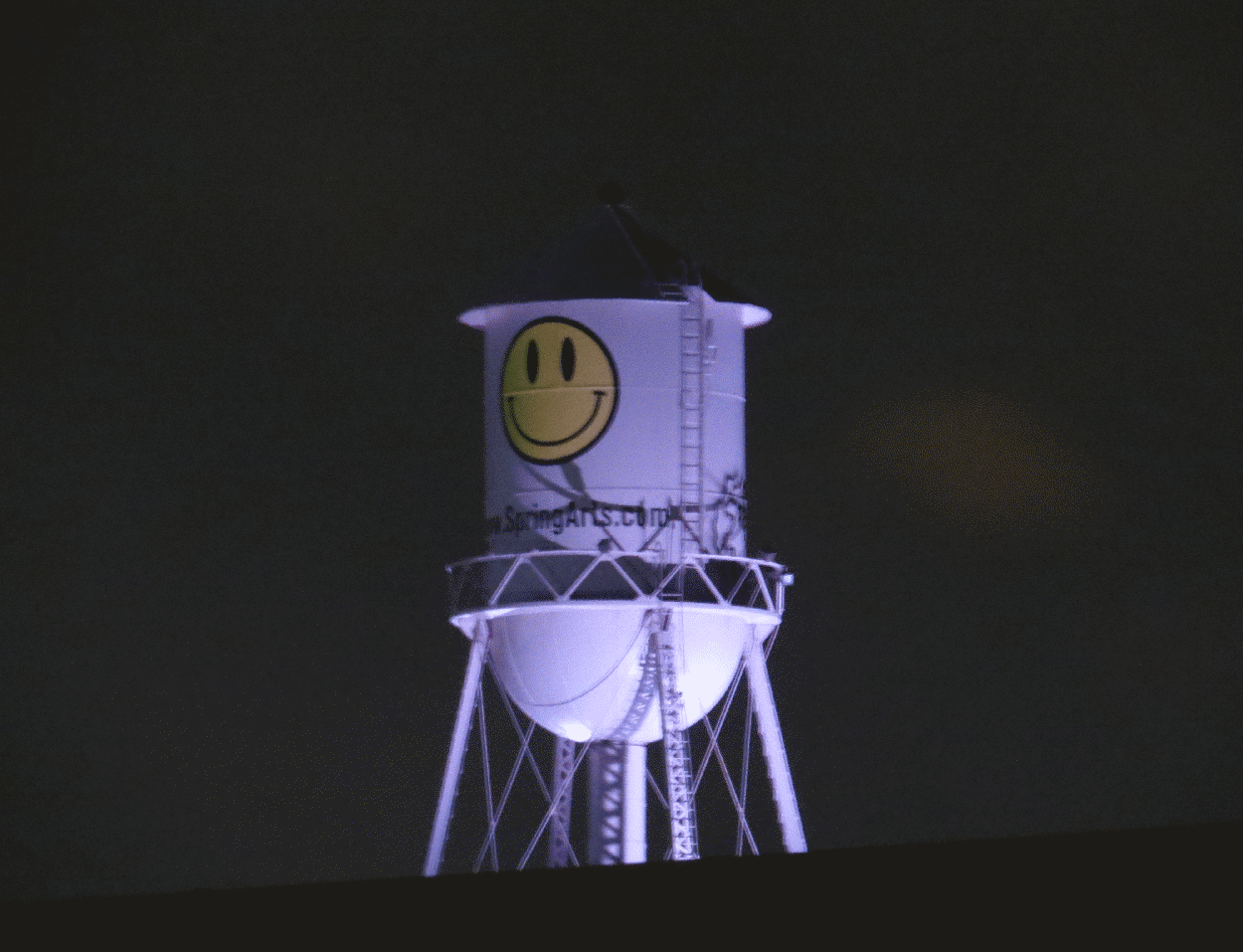 A watertower with a yellow smiley-face on it.