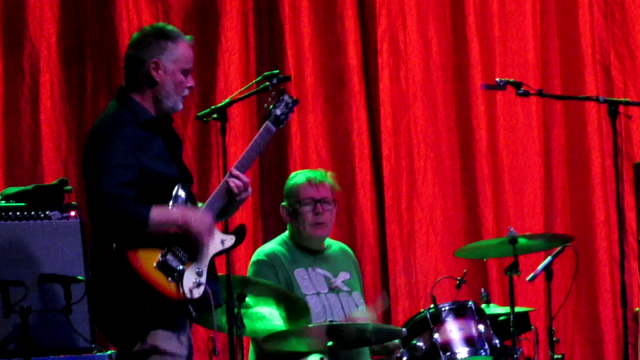Tim Gane playing guitar and Andy Ramsay playing drums.